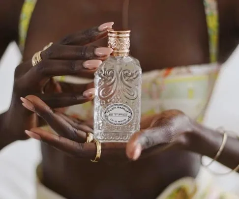 Hands holding an intricately designed Etro perfume bottle with detailed patterns.