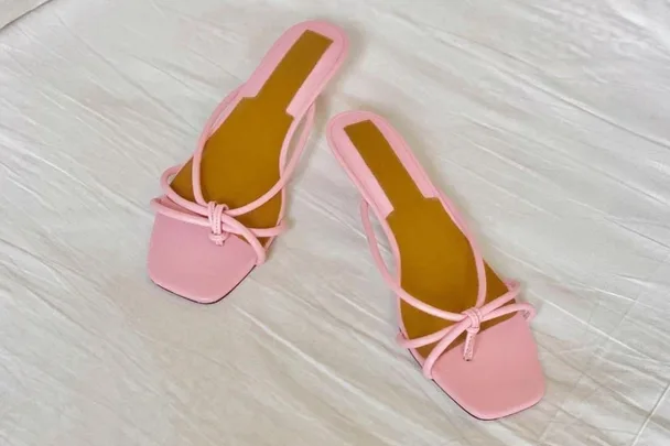 Pink square-toe sandals with thin straps on a white surface.