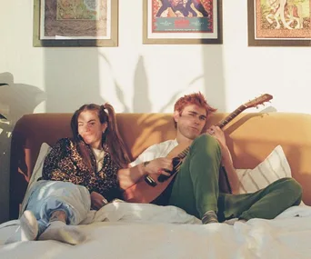 Couple relaxing on bed with guitar; surrounded by colorful wall art.