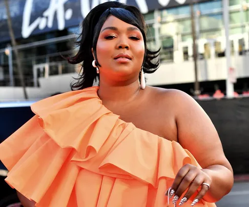 A person poses in an orange ruffled dress outdoors with a blurred building in the background.