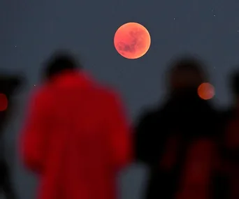 Total lunar eclipse with red moon and silhouettes of observers in the foreground.