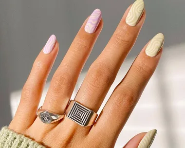 Hand with psychedelic-marble nails in pastel shades, wearing silver geometric rings.