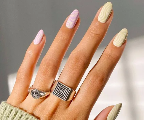 Hand with psychedelic-marble nails in pastel shades, wearing silver geometric rings.