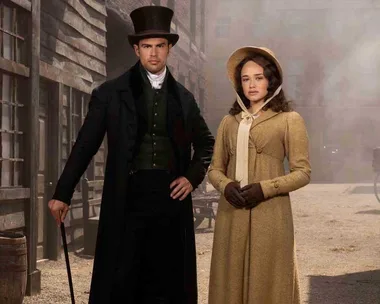 A man and a woman in period costumes stand in a dusty street setting from "Sanditon" Season 2.