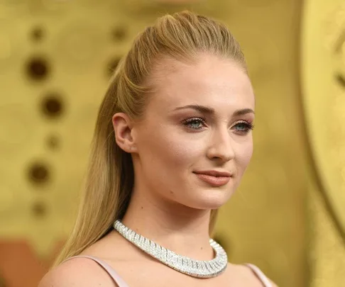 A woman with long hair pulled back, wearing a silver necklace against a blurred golden backdrop.