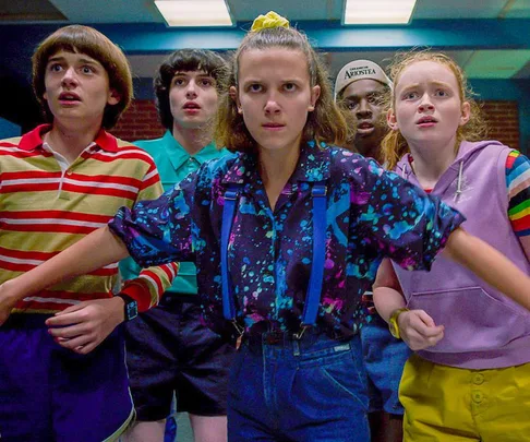 Group of five youths look determined, led by a girl in a patterned shirt. Scene from Stranger Things Season 3.