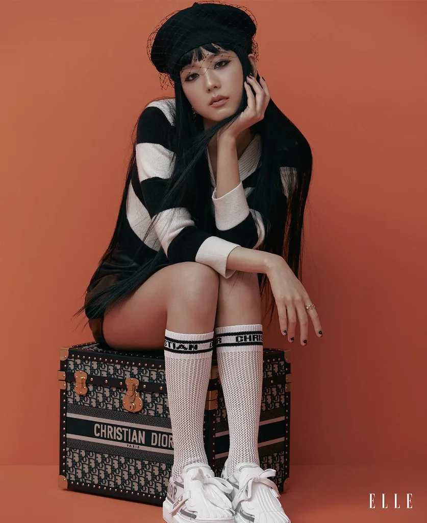 Jisoo seated on a Dior trunk in a black beret, striped sweater, skirt and white Dior-ID sneakers.