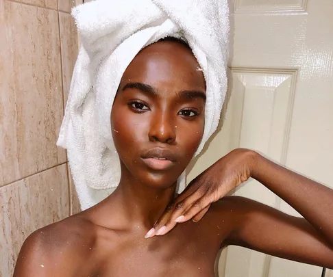 A person with a towel wrapped around their head poses confidently against a bathroom door.