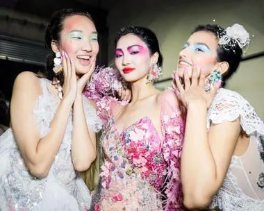 Three models in vibrant makeup and floral dresses pose together at Australian Fashion Week 2021.