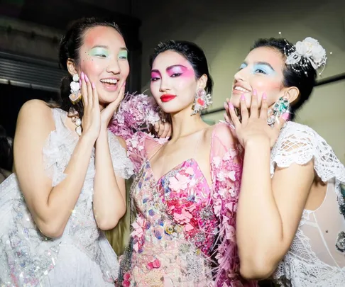 Three models in vibrant makeup and floral dresses pose together at Australian Fashion Week 2021.