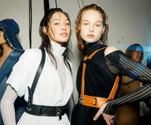 Models backstage at Australian Fashion Week 2021 wearing harnesses over monochrome outfits, with wet-look hair.