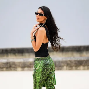 Woman in sunglasses, black top, green snakeskin pants at Paris Fashion Week Spring 2022, looking over shoulder.