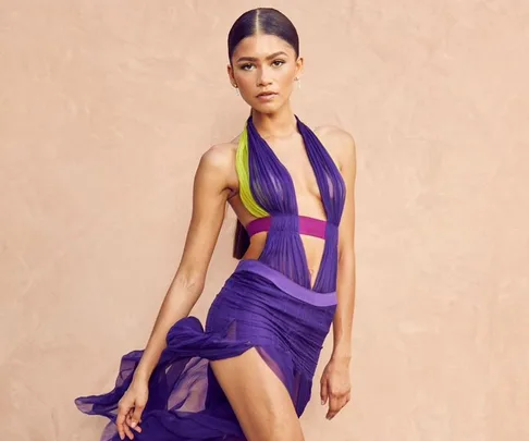 Woman in a colorful purple and green dress on a beige background, posing on the BET Awards 2021 red carpet.