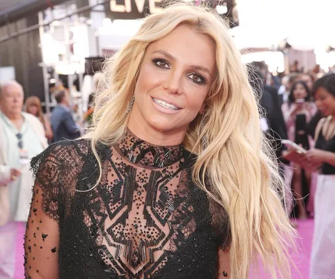 Britney Spears smiling, wearing a black lace dress on a red carpet event.