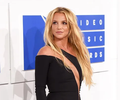 A woman with long blonde hair in a black dress at a red carpet event, standing in front of a "Video Music Awards" sign.