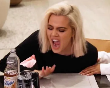 A person with blonde hair, sitting at a table, laughing with mouth open, next to a bottle of Diet Snapple.