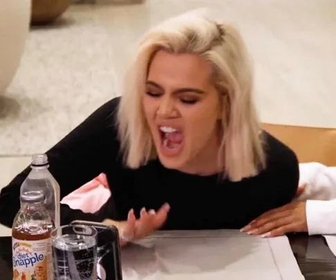 A person with blonde hair, sitting at a table, laughing with mouth open, next to a bottle of Diet Snapple.