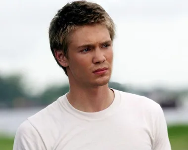 Young man with short hair wearing a white t-shirt, standing outdoors with a serious expression.