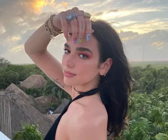 Person posing outdoors at sunset with colorful nail art and jewelry.