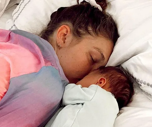 Woman and baby sleeping together on a bed, wrapped in colorful duvet.