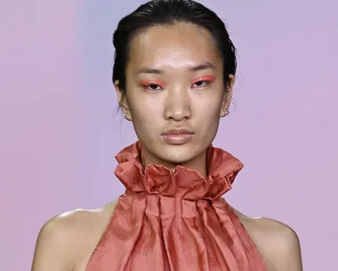 Model on runway at Australian Fashion Week 2021, wearing a red ruffled outfit and pastel eye makeup.