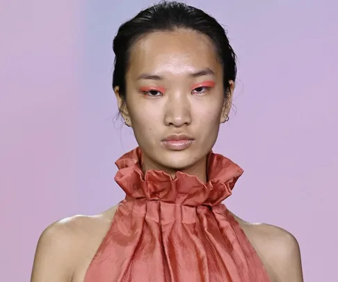 Model on runway at Australian Fashion Week 2021, wearing a red ruffled outfit and pastel eye makeup.