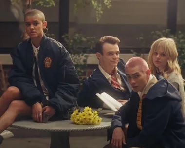 Four students sit at a table with a bouquet of yellow flowers, wearing school uniforms.