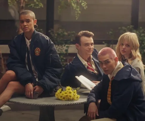 Four students sit at a table with a bouquet of yellow flowers, wearing school uniforms.