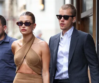 A fashionable couple wearing sunglasses and stylish outfits walk together on a city street.