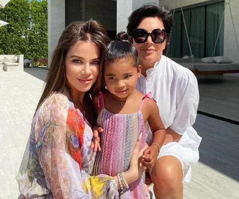 Three people posing happily outdoors, including a child in a colorful dress, with modern patio furniture in the background.