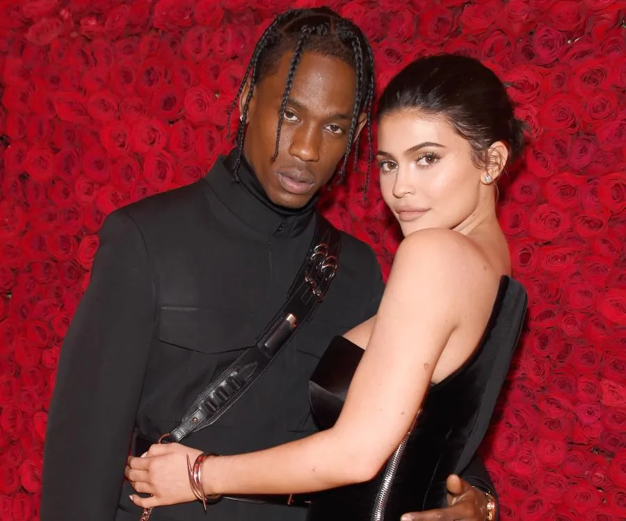 A couple poses in front of a red rose wall, embracing each other warmly.