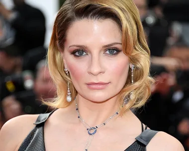 A woman with short blonde hair and blue eyes wearing a black dress and silver jewelry at a public event.