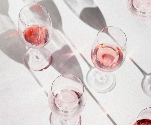 Five glasses of pink wine casting shadows on a white surface.