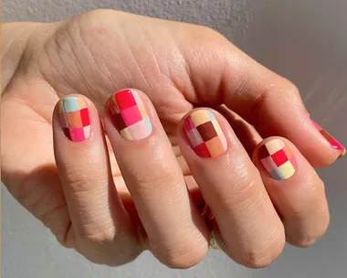 Close-up of a hand with vibrant plaid nail art featuring various colors like pink, blue, and yellow.