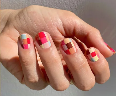 Close-up of a hand with vibrant plaid nail art featuring various colors like pink, blue, and yellow.