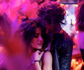 A man and woman share an intimate moment in a dimly lit, vibrant nightclub setting.