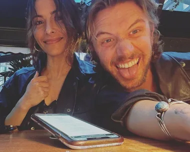 A woman smiling and a man making a playful face at a restaurant table with a phone in front of them.