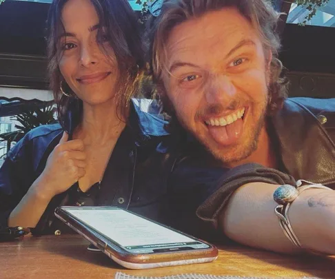 A woman smiling and a man making a playful face at a restaurant table with a phone in front of them.