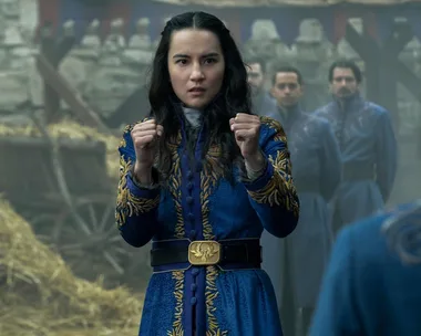 A character in a blue embroidered coat stands in a fighting stance, with people in similar blue uniforms behind her.