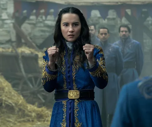 A character in a blue embroidered coat stands in a fighting stance, with people in similar blue uniforms behind her.