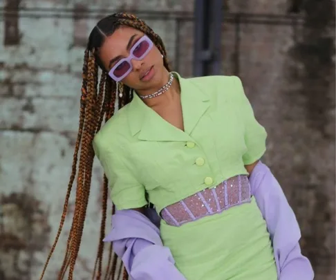 Person in lime green outfit with purple sunglasses and long braided hair at Australian Fashion Week 2021.