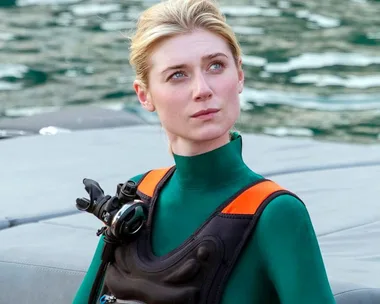 Woman in a green wetsuit with scuba gear on a boat, looking thoughtful.