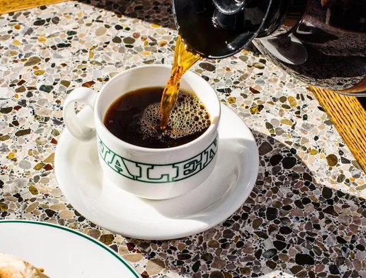 Coffee being poured into a white cup with "VALET" on a terrazzo table at a Sydney café.