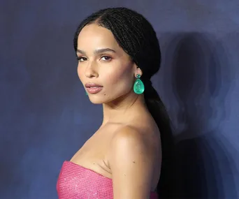 Zoe Kravitz in a strapless pink dress with green earrings against a dark background.