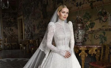 Bride in elegant lace wedding gown with long sleeves, standing in ornate room with historic decor.