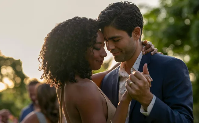 A couple gently dancing outdoors at sunset, close and smiling, with soft focus greenery in the background.