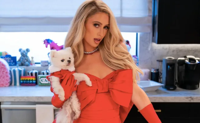 Person in a red dress holding a white dog in a kitchen setting.