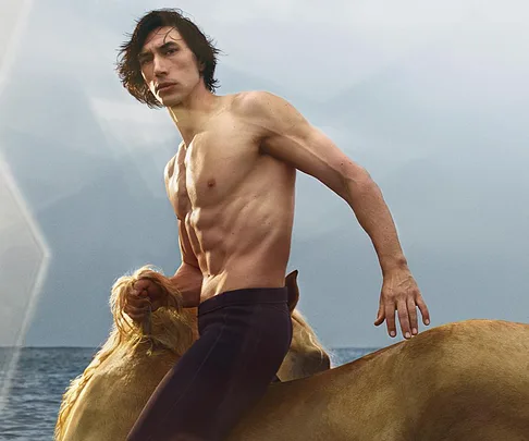 Shirtless man with lean physique riding a horse by the sea under a cloudy sky.