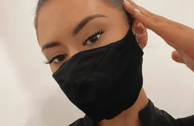 Person wearing a black silk face mask, touching face with one hand, showing eyebrows and eyelashes.