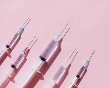 Syringes aligned on a pink background, illustrating preparation for Botox treatment.